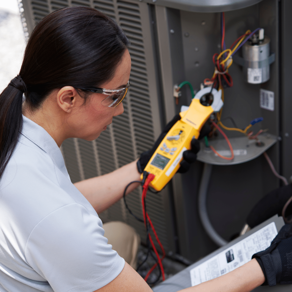 female technician holding device thats connected to outdoor hvac unit while looking at a piece of paper