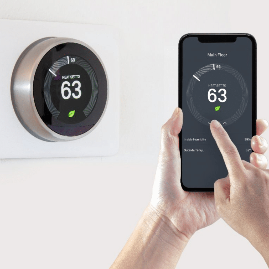 smart thermostat positioned on wall with hand holding phone controlling the thermostat in front of it