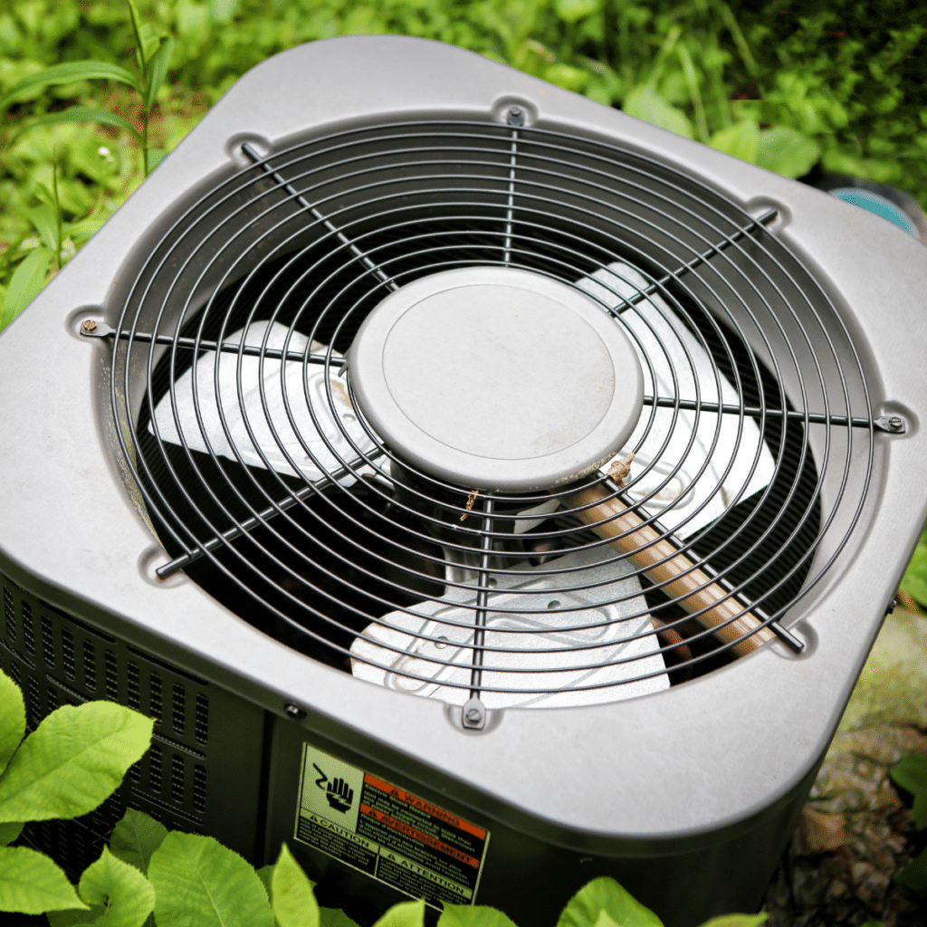 closeup of the top of an outdoor hvac unit surrounded by green leaves