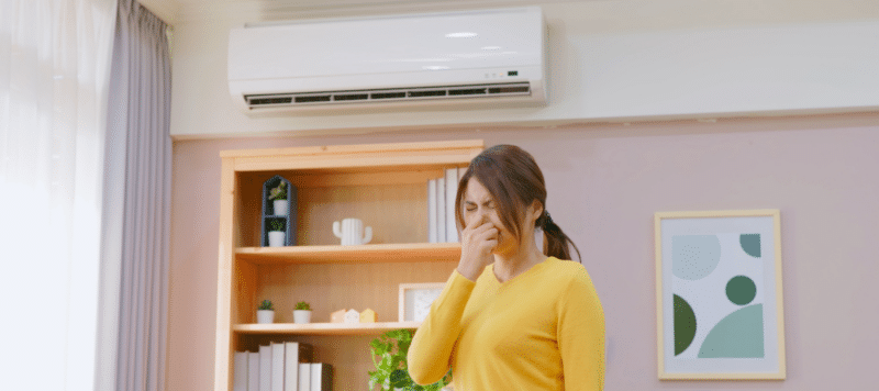 woman holding her nose due to a bad smell with a ductless ac system installed above her
