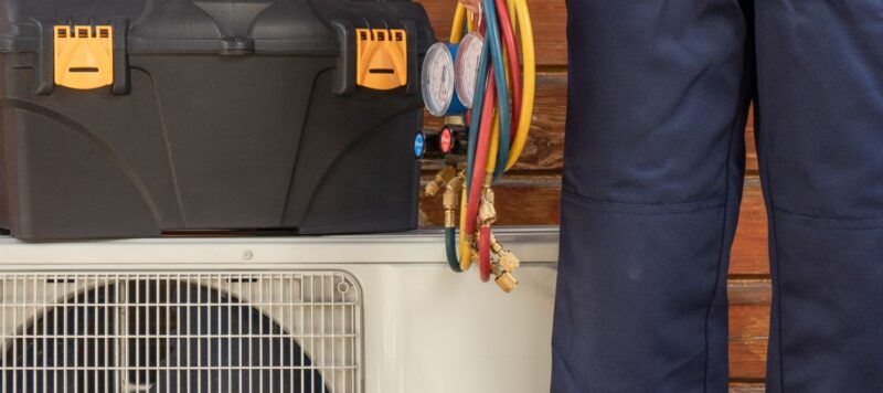 a toolbox on top of an outdoor ac unit with an ac technician standing next to it and holding equipment