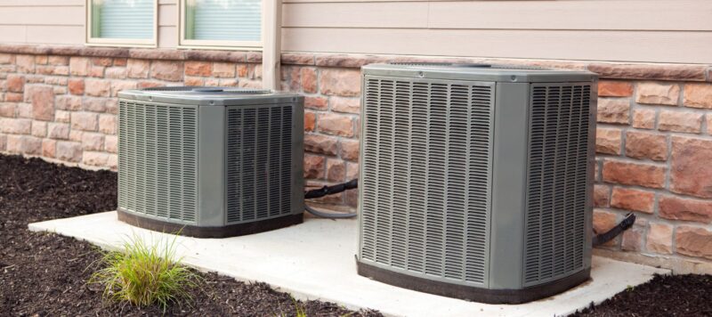 two outdoor hvac units against the side of a pink home
