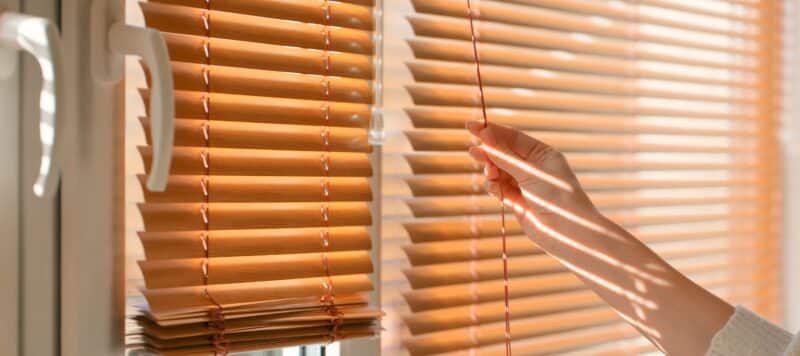 person's hand reaching up to twist the stick on blinds to open and close them