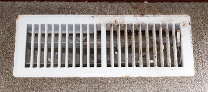 closeup of a white floor vent with mold and dust on it