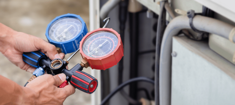 Technician using HVAC pressure gauges to monitor and adjust refrigerant levels