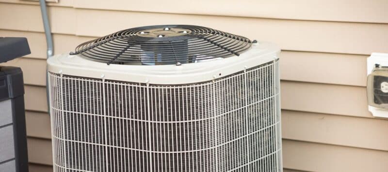 Outdoor air conditioning unit next to a house siding wall, showing the fan and condenser coil